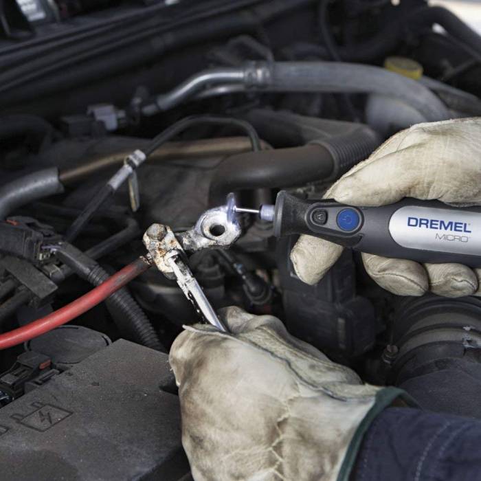 mechanic using a cordless dremel tool to clean a car battery terminal